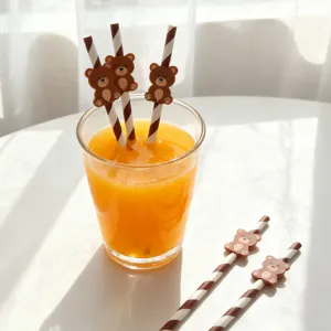 Detailed view of striped paper drinking straws with cute brown bear decorations in a glass of juice.