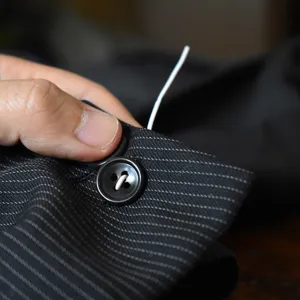 Detail view of fast button fixing tool attaching a black button to striped suit fabric.