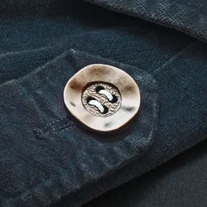 Detail shot of a retro four-hole button sewn on dark textured fabric for clothing.