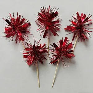 Close-up of red tinsel cake toppers, shiny metallic foil firework party picks for dessert decor.