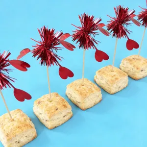 Close-up of red heart tinsel decorative picks inserted in square pastries, party dessert setup.