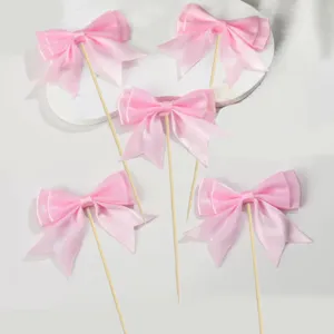 Close-up detail of pink double-layer bow cake toppers on wooden sticks for party decor.