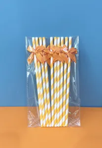 Vista dettagliata di cannucce di carta a righe gialle e bianche con fiocchi arancioni trasparenti.