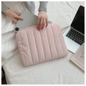 Detailed view of pink quilted laptop sleeve with vertical stripe design on white bed.
