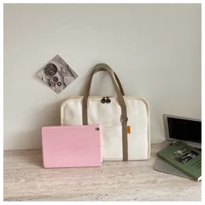 Vista dettagliata di una borsa per laptop in tela beige con spallacci marroni su una scrivania.