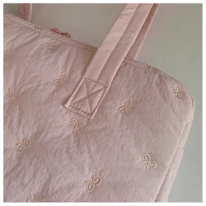 Gros-plan d'un sac cabas matelassé rose pour ordinateur avec de jolis nœuds brodés.