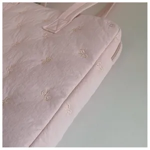Vue détaillée d'un joli sac pour ordinateur portable rose matelassé avec des nœuds brodés.