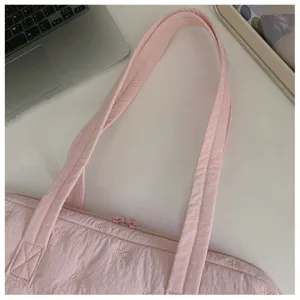 Gros plan détaillé d'un sac pour ordinateur matelassé rose avec nœuds brodés et texture.