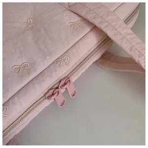 Vue en gros plan de la housse d'ordinateur matelassée rose avec de jolies broderies de nœuds.