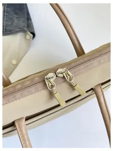 Close-up detail of minimalist beige laptop bag zipper and leather handles, elegant design.