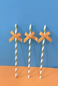 Primo piano di cannucce di carta rigate con fiocchi in nastro arancione per decorare feste.