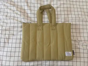 Quilted laptop bag detail showing fabric texture, sturdy handles, and branded woven tag.