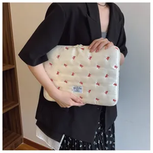 Detail shot of 14-inch quilted laptop sleeve featuring cute red bow embroidery and portable design.