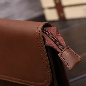 Detalle de un bolso de mano vintage para hombre en cuero marrón con costuras finas.