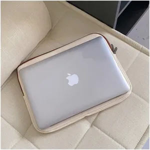 Close-up view of a minimalist beige laptop sleeve with brown trim placed on a cozy sofa.