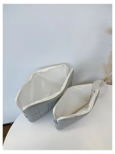 Detail shot of grey quilted cosmetic zipper storage pouches set on clean white table surface.