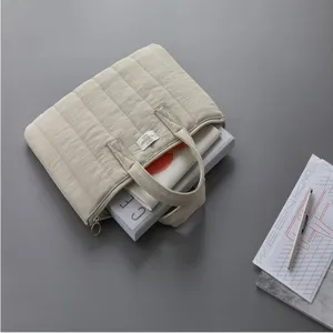 Detail view of beige quilted laptop sleeve with handles, elegant minimalist style.