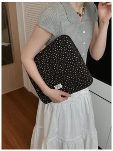 Detailed view of a black quilted floral laptop sleeve held by a model, perfect for 13 inch devices.