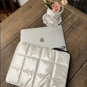 Dettaglio della custodia per laptop trapuntata bianca su tavolo in legno, morbida e protettiva.