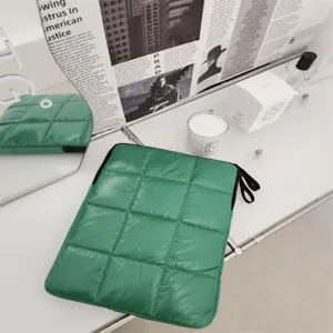 Dettaglio custodia trapuntata verde per laptop, texture morbida e allestimento da scrivania.