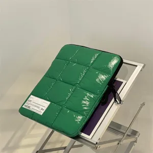 Dettaglio di una custodia per laptop verde trapuntata lucida con design a griglia imbottita.