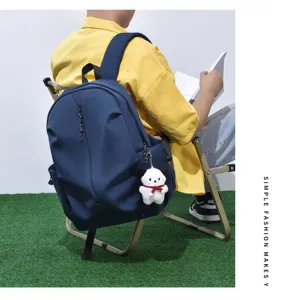 Detail view of a casual blue backpack worn by a model sitting on a chair, showing large capacity.