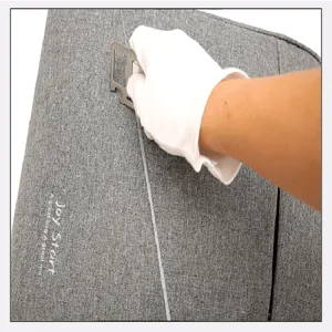 Grey fabric backpack detail view showing wear-resistant material test with metal tool surface.