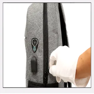 Backpack detail view showing grey fabric texture, USB charging port, and smooth zipper.