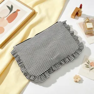 Detailed view of black and white striped cosmetic bag with cute ruffle trim on white background.