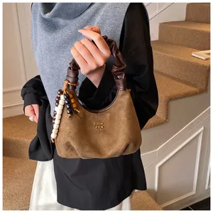 Brown suede hobo handbag detail shot, featuring pleated handle and decorative wooden beaded charm.