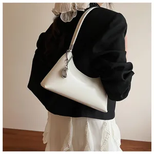 Stylish white underarm shoulder bag detail showing chic pillow design and metallic charm pendant.