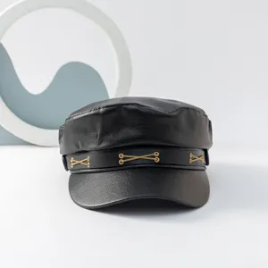 Nahaufnahme der schwarzen PU-Leder Schiebermütze mit goldenen Kreuzketten-Details.