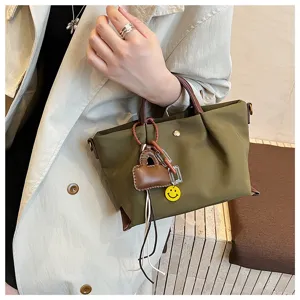Green nylon handbag close-up showing brown leather handle and cute smiley face pendant detail.