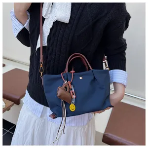 Close-up detail of blue nylon crossbody bag featuring brown handles and cute charms.