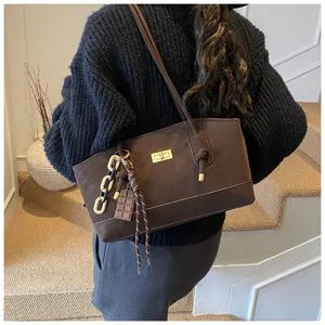 Brown commuter shoulder bag detail, featuring unique chain charm and elegant golden hardware.