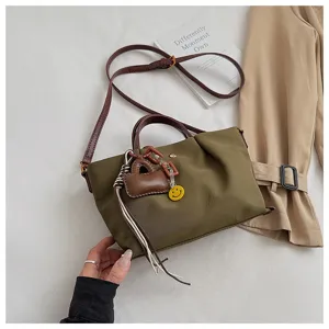 Close-up detail view of the olive green canvas crossbody bag with charm pendants and strap.
