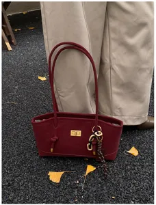 Burgundy tote bag detail showing gold turn-lock closure, knotted straps and pebbled texture.