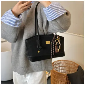 Detail shot of a black shoulder bag with a gold turn-lock and cute charms, casual commuter style.