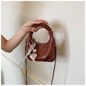 Detailansicht der braunen gerafften Handtasche mit weicher Ledertextur, schicker Kette und süssen Anhängern.