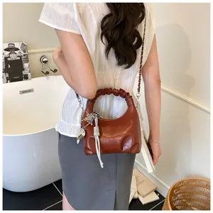 Detailaufnahme einer braunen Schultertasche mit Raffung am Modell, texturierter Griff.