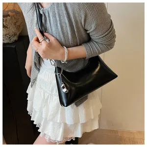 Detail shot of a chic black patent leather shoulder underarm bag with metal chain accent.
