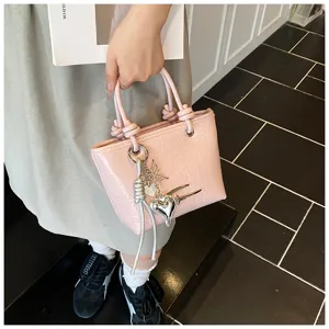 Pink glossy leather handbag detail featuring cute silver charms and stylish handles.