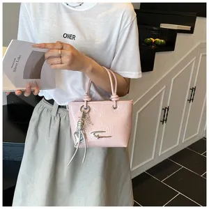 Detail shot of stylish pink glossy mini handbag with metal logo and silver charms for women.