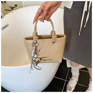 Detailed view of the glossy beige small handbag with metal charms and top handles in use.