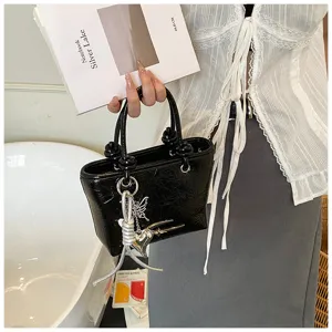 Black glossy textured handbag with metal heart and butterfly charms for women daily street style.