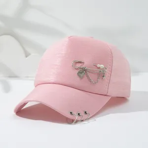 Roze honkbalpet detail met veiligheidsspeld kettingen, parels en metalen ringen.