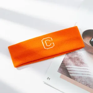 Primer plano detallado de diadema deportiva de punto naranja brillante con letra C bordada blanca.