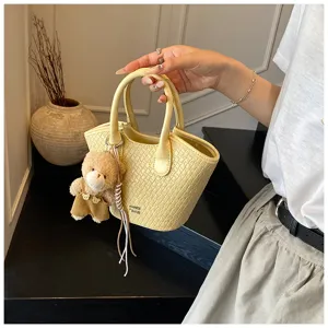 Detail view of the yellow bucket bag with cute bear charm and crocodile pattern texture.