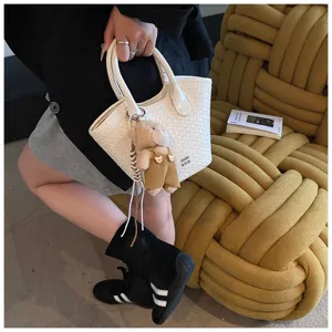 White woven handbag for women stylish small bucket bag with cute bear pendant detail.