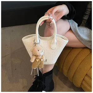 Detail shot of white woven basket handbag featuring a cute plush teddy bear keychain charm.